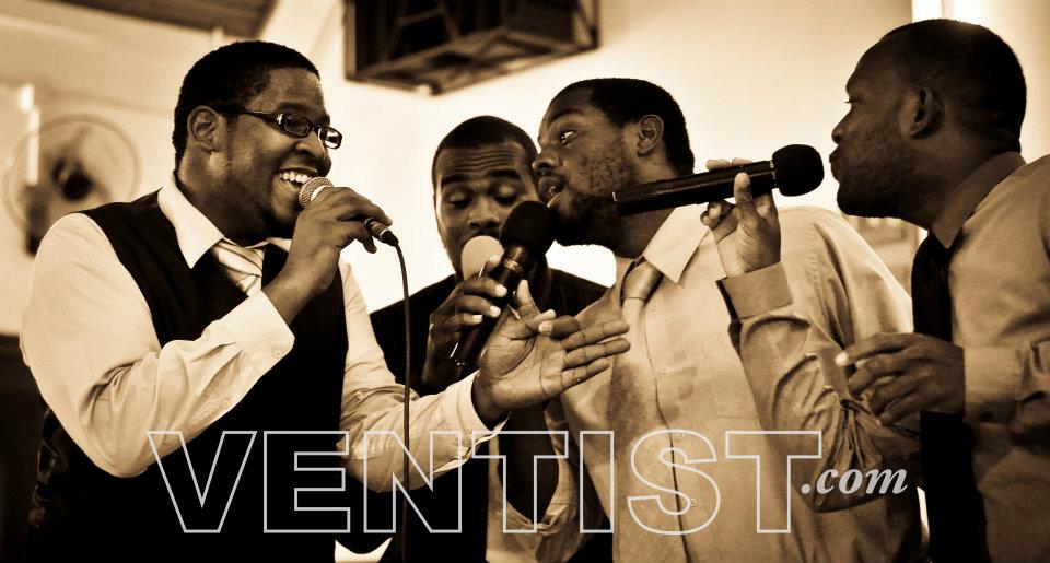 Four men singing together into microphones